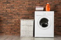 Modern washing machine with stack of towels, detergent and laundry basket near wall Royalty Free Stock Photo