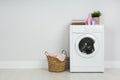 Modern washing machine with stack of towels, detergents and laundry basket near wall. Space for text Royalty Free Stock Photo