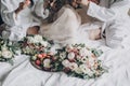 Modern wedding bouquets, wedding rings and delicious macarons on white bed on background of bride and bridesmaids celebrating. Royalty Free Stock Photo