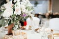 MOdern wedding decor - guest tables with white tableclothes, golden plates, white roses and eucalyptus leaves floral arrangements Royalty Free Stock Photo