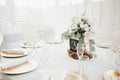 MOdern wedding decor - guest tables with white tableclothes, golden plates, white roses and eucalyptus leaves floral arrangements Royalty Free Stock Photo