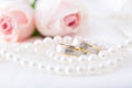 Modern wedding rings with pearl necklace wih pink roses in the background Royalty Free Stock Photo