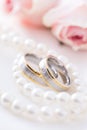 Modern wedding rings with pearl necklace wih pink roses in the background Royalty Free Stock Photo