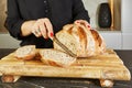 Landlady slicing bread on wooden board in marble kitchen with knife in hands