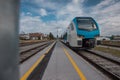 Modern white and blue passenger train coming towards a stop in station in front of a modern housing or residental district