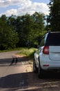 A modern white car sits at the edge of the road next to a green field while traveling and looking for new routes. Outdoor weekends