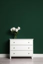 Modern white chest of drawers with bouquet near green wall indoors Royalty Free Stock Photo