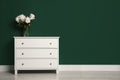 Modern white chest of drawers with beautiful bouquet near green wall indoors. Space for text Royalty Free Stock Photo