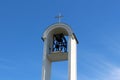 Modern white church bell tower with large open metal bell mechanism and shiny steel cross on top with clear blue sky in background Royalty Free Stock Photo