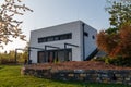 Modern, white, cube, elegant, minimalist style passive house with large panoramic windows, grey shutters in maintained garden in Royalty Free Stock Photo