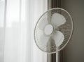 White Electric Fan Stands Near Bright Window Curtains Royalty Free Stock Photo
