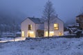 Modern white house with light windows surronded by mountain, snow and trees. Chirstmas mood