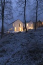 Modern white house with light windows surronded by mountain, snow and trees. Chirstmas mood