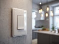 Modern white light switch mounted on textured wall with blurred view of warm-lit contemporary kitchen interior in the background Royalty Free Stock Photo