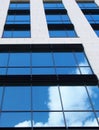 Modern white office building with mirrored glass windows reflecting a bright blue sky and white clouds Royalty Free Stock Photo