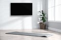 Modern wide screen TV on white wall in room with yoga mat