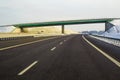 Modern wide smooth empty asphalt highway stretching to horizon under high bridge turning right past distant forest at day. Speed, Royalty Free Stock Photo