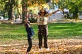 A modern woman joyfully plays with her son in the park, tossing leaves on a beautiful autumn day, capturing the essence