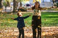 A modern woman joyfully plays with her son in the park, tossing leaves on a beautiful autumn day, capturing the essence