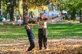 A modern woman joyfully plays with her son in the park, tossing leaves on a beautiful autumn day, capturing the essence