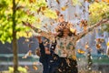 A modern woman joyfully plays with her son in the park, tossing leaves on a beautiful autumn day, capturing the essence