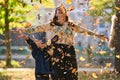 A modern woman joyfully plays with her son in the park, tossing leaves on a beautiful autumn day, capturing the essence