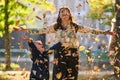 A modern woman joyfully plays with her son in the park, tossing leaves on a beautiful autumn day, capturing the essence