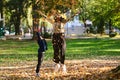 A modern woman joyfully plays with her son in the park, tossing leaves on a beautiful autumn day, capturing the essence