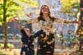 A modern woman joyfully plays with her son in the park, tossing leaves on a beautiful autumn day, capturing the essence