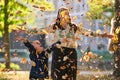 A modern woman joyfully plays with her son in the park, tossing leaves on a beautiful autumn day, capturing the essence