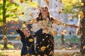 A modern woman joyfully plays with her son in the park, tossing leaves on a beautiful autumn day, capturing the essence