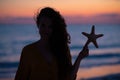 Modern woman on ocean coast at sunset holding starfish