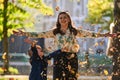 A modern woman joyfully plays with her son in the park, tossing leaves on a beautiful autumn day, capturing the essence