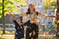 A modern woman joyfully plays with her son in the park, tossing leaves on a beautiful autumn day, capturing the essence