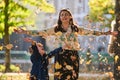 A modern woman joyfully plays with her son in the park, tossing leaves on a beautiful autumn day, capturing the essence