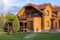 Modern wooden eco house villa facade luxury big house. Timber cottage with with green lawn water sprinkler, paved