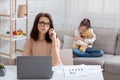 Modern working mom doing online job, her neglected daughter hugging teddy bear, feeling lonely and sad at home Royalty Free Stock Photo