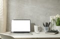 Modern working space with laptop, books, table lamp and stationery by the window with sun shade roller blind