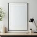 Modern workspace with blank picture frame, desk lamp, and plant on wooden table against a white wall Royalty Free Stock Photo