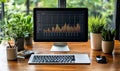 modern workspace with computer monitor displaying financial graph surrounded by green plants on wooden desk near window Royalty Free Stock Photo