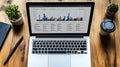 a modern workspace with a laptop displaying colorful bar charts and graphs surrounded by plants a pen and a coffee cup Royalty Free Stock Photo