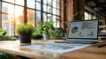 modern office workspace with laptop showing business charts and graphs near green plant on wooden table with sunlight Royalty Free Stock Photo