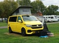 Modern Yellow Volkswagen Camper Van with high top up and awning on campsite.