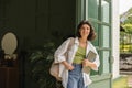 Modern young caucasian female student with backpack, laptop stands outdoors.