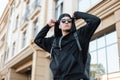 Modern young handsome hipster man in a fashionable sweatshirt with stylish sunglasses in a cap with a trendy backpack posing Royalty Free Stock Photo