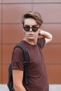 Modern young hipster man with a fashionable hairstyle in black stylish sunglasses in a summer t-shirt with a sports black backpack Royalty Free Stock Photo