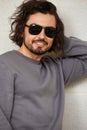 Modern young man in sunglasses with long hair, handsome man in glasses on the background of the wall, smiling, lifstyle.