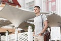 Modern young stylish man freelancer in a leather trendy bag in a fashionable striped t-shirt with a hairstyle stands
