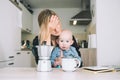 Modern tired mother and little child after sleepless night. Exhausted woman with baby is sitting with coffee in kitchen. Life of Royalty Free Stock Photo