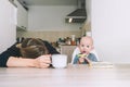 Modern tired mother and little child after sleepless night. Exhausted woman with baby is sitting with coffee in kitchen. Life of Royalty Free Stock Photo